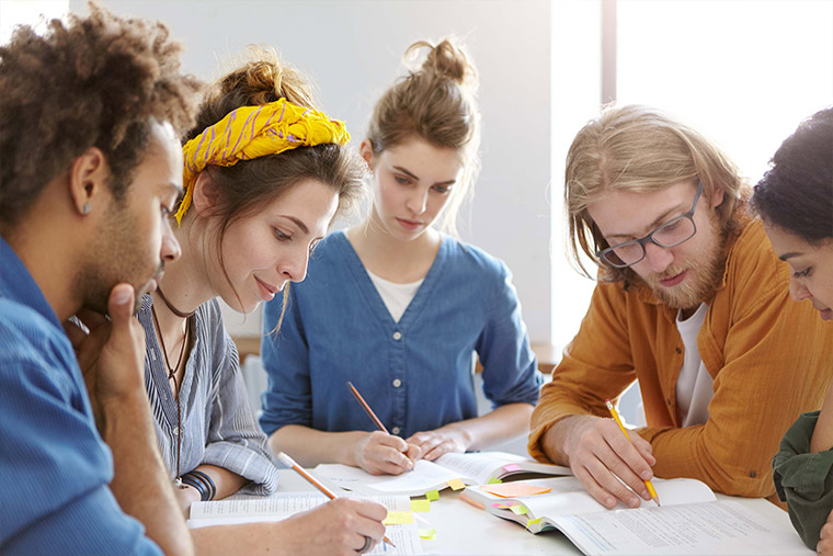 Four teenagers collaborating on paper work around a table