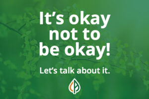 Tree leaf branches with the words "Its okay not to be okay!" on top with "Let's talk about it" at the bottom