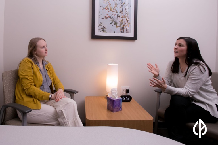 A peer support specialist listens intently as a person across a table from them speaks.