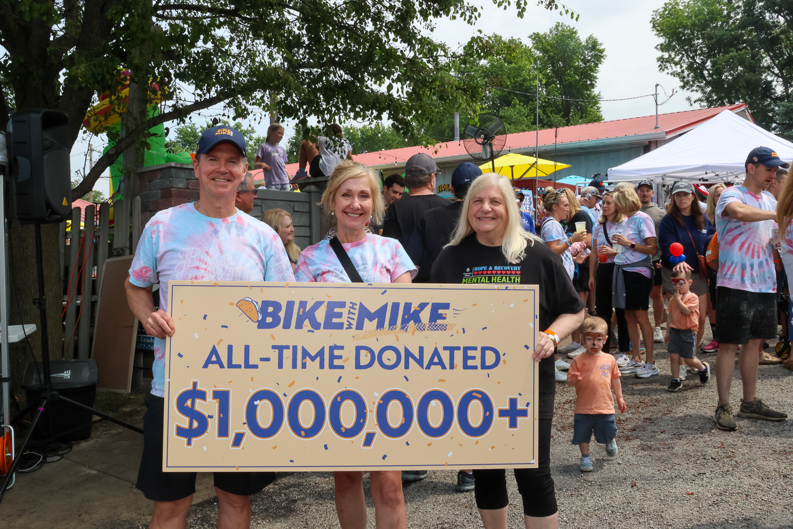 Canon EOS R7 Kutilek family and Community Alliance CEO hold up check stating, "Bike with Mike all-time donated $1,000,000".