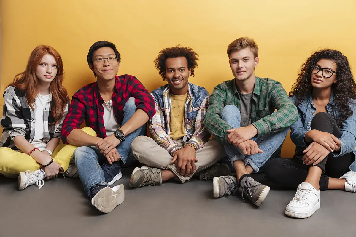 Multiethnic group of smiling young friends sitting over yellow