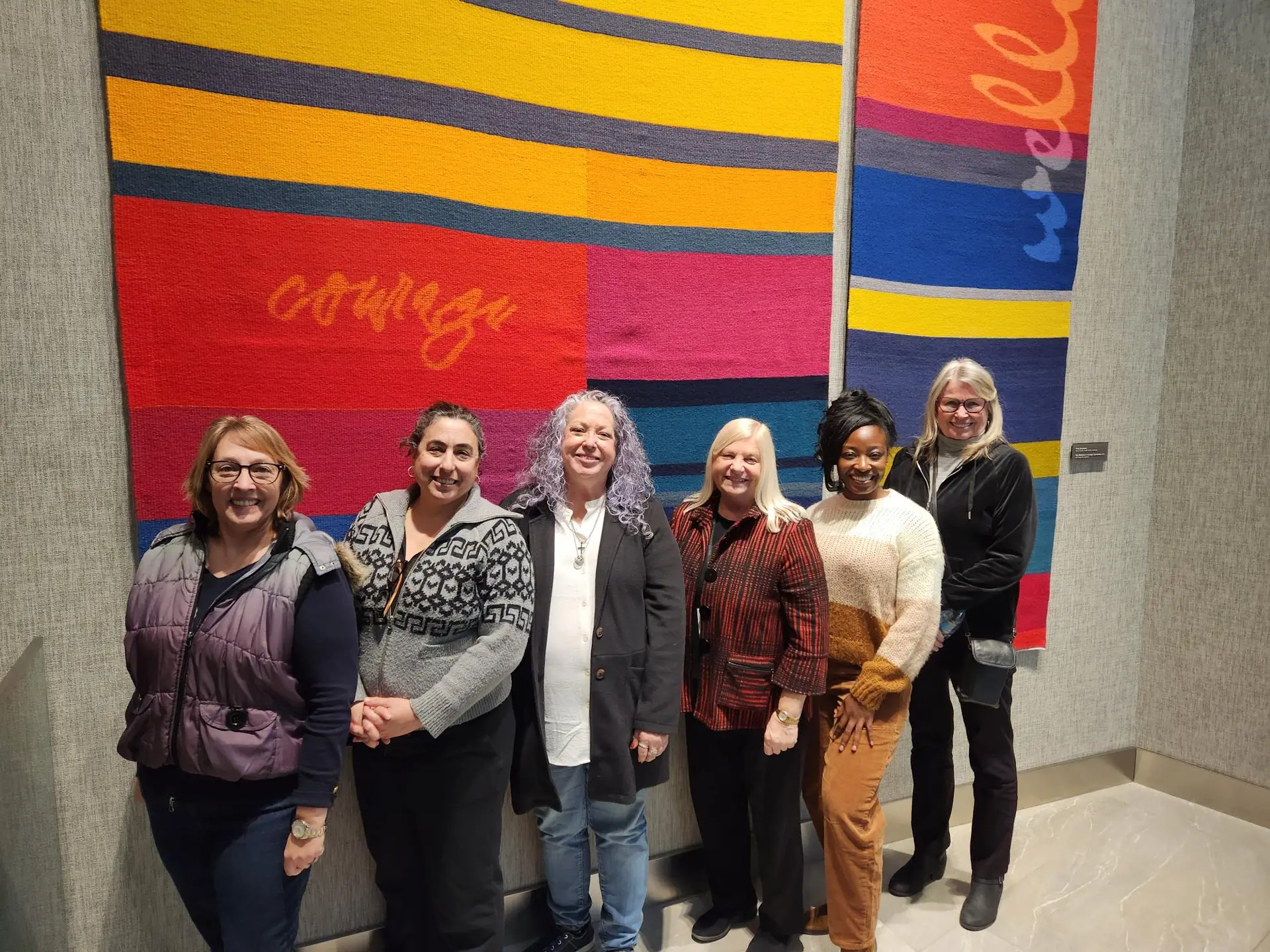 Aileen Brady stands with the CARF accreditation surveyors in front of several tapestries at Community Alliance's headquarters.